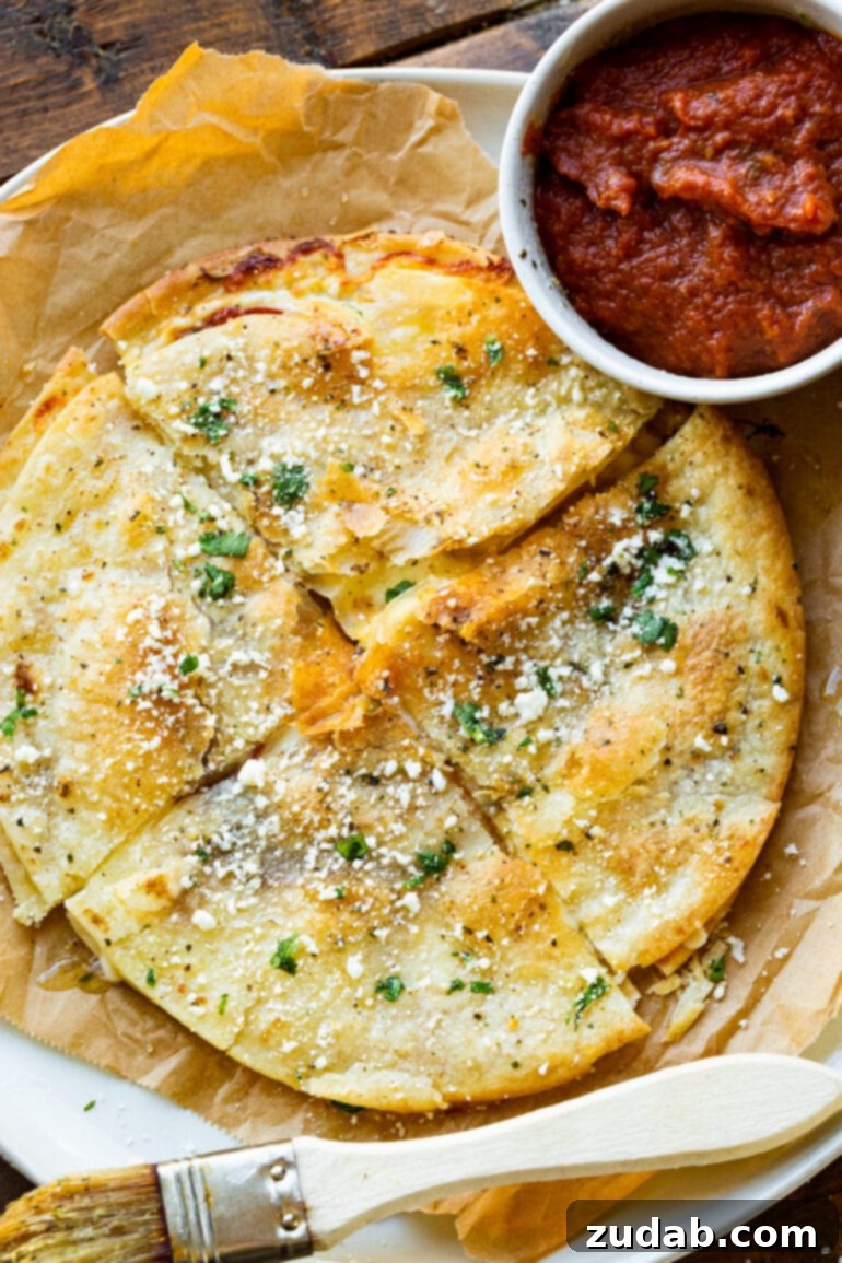 Pizza-dilla: A Cheesy Pizza Quesadilla 3 A full, golden-crispy tortilla pizza, perfectly quartered, generously topped with savory garlic butter and sprinkled cotija cheese, with a small dish of pizza sauce nearby.