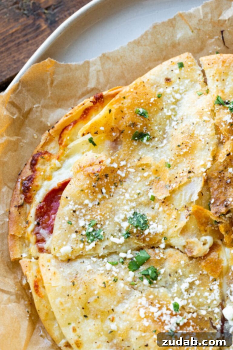 Pizza-dilla: A Cheesy Pizza Quesadilla 4 A close-up photo of a crispy, golden tortilla pizza, showcasing abundant melted mozzarella and perfectly browned pepperoni slices spilling out from the sides.