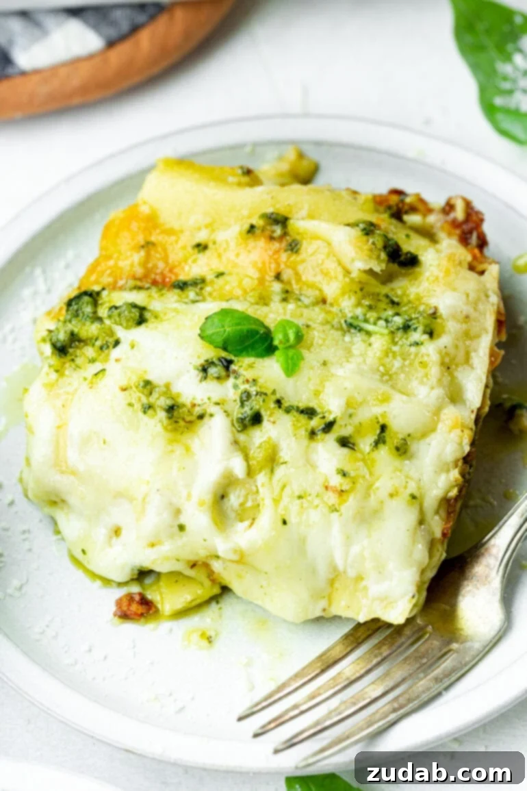 Effortless Creamy Pesto Chicken Lasagna 4 A generous serving of creamy pesto chicken lasagna on a white plate, with a fork poised for a bite, emphasizing its delicious appeal.