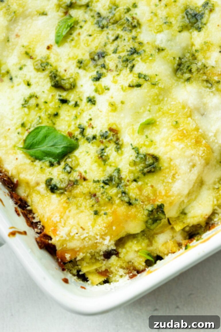 Effortless Creamy Pesto Chicken Lasagna 6 A creamy baked pesto chicken lasagna in a white ceramic baking dish, garnished with a fresh basil leaf and pesto drizzles, ready to serve.