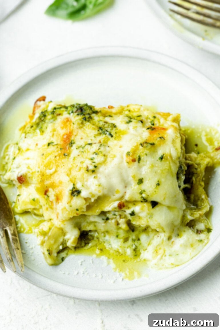 Effortless Creamy Pesto Chicken Lasagna 7 A single serving of creamy pesto chicken lasagna resting on a pristine white dinner plate, highlighting its appetizing presentation.