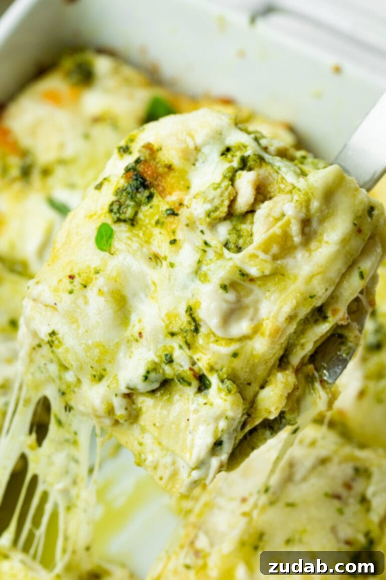 Effortless Creamy Pesto Chicken Lasagna 10 A serving of creamy chicken pesto lasagna being carefully lifted from a casserole dish with a spatula, showcasing its inviting layers.