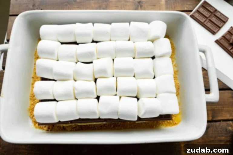 Gooey Smores Sliders 5 The bottom halves of a dozen slider buns, perfectly aligned in a baking dish, are generously topped with Hershey's chocolate bars and then a layer of large, fluffy marshmallows, ready for the top buns.