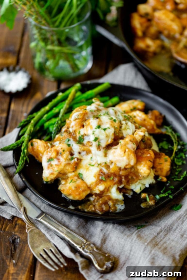 Weekly Meal Plan - Mar. 25 to Mar. 31 5 A stunning close-up photo of a plate of French onion chicken. The tender chicken breast is richly topped with a generous layer of deeply caramelized onions and melted Gruyere cheese, which glistens under the light. A side of perfectly cooked green asparagus spears provides a vibrant contrast and completes the elegant presentation of this delicious dish.