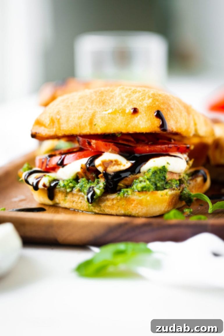 Weekly Meal Plan - Mar. 25 to Mar. 31 8 A beautifully presented chicken caprese sandwich, cut in half and stacked to showcase its mouth-watering layers. Inside a rustic ciabatta bun, you can see tender grilled chicken, juicy tomato slices, creamy fresh mozzarella, vibrant green pesto, and a glossy drizzle of balsamic glaze. This image captures the gourmet appeal and fresh ingredients of the sandwich, making it highly appetizing.