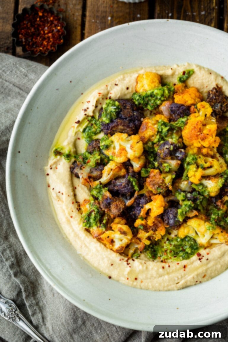 Crispy Roasted Cauliflower with Creamy Hummus 2 a photo of roasted white and purple cauliflower florets on top of a bowl full of hummus and topped with pesto sauce