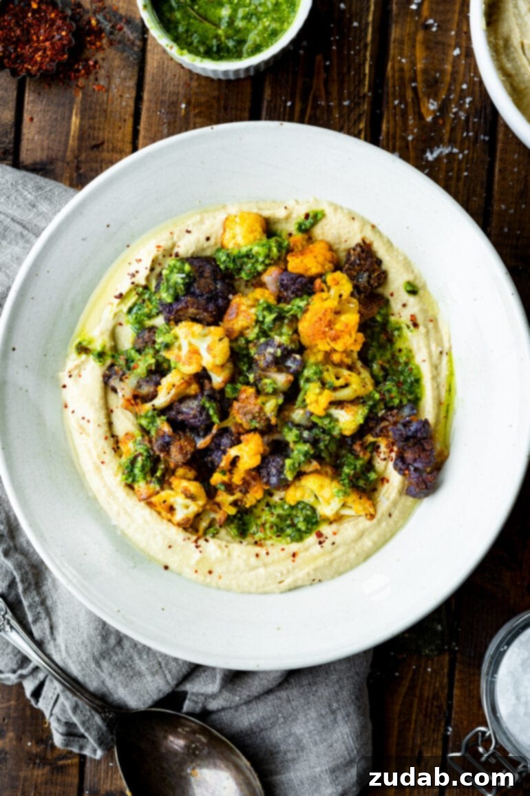 Crispy Roasted Cauliflower with Creamy Hummus 7 a photo taken over the top of a serving plate full of creamy hummus topped with roasted tricolor cauliflower florets.