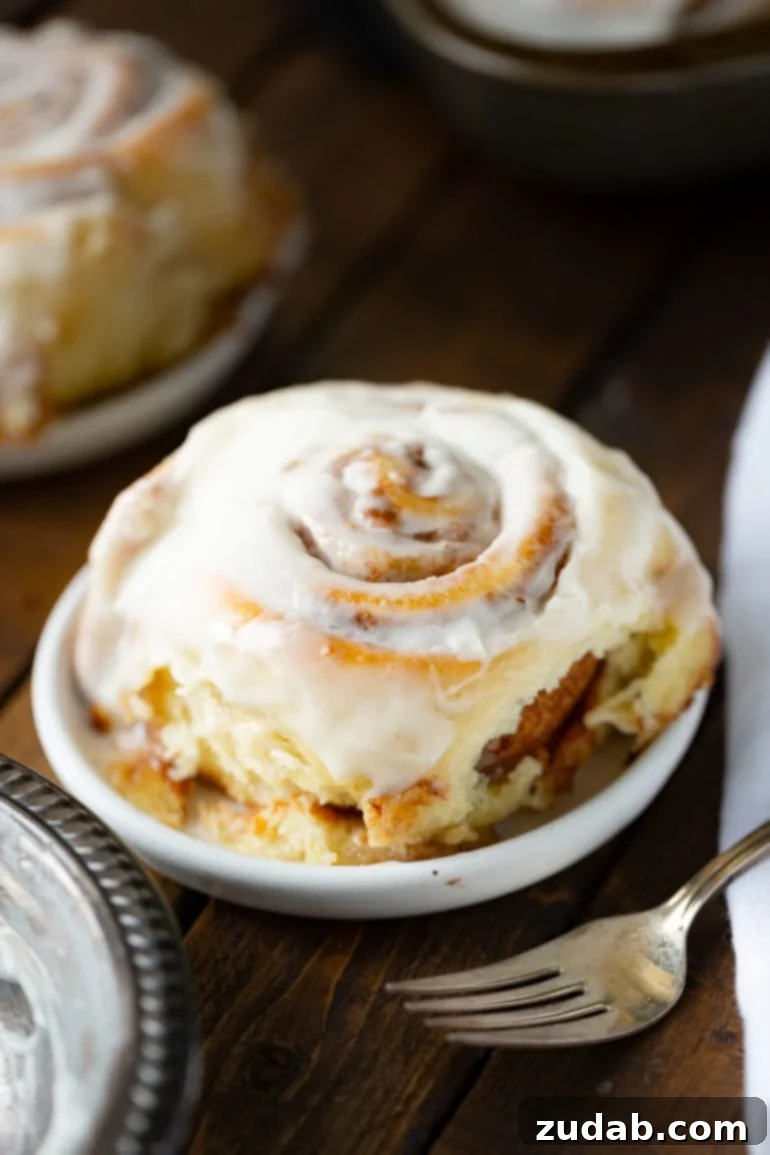 Your Ultimate Easter Sunday Feast 3 a photo of a single cinnamon roll topped with a creamy white frosting sitting on a small dessert plate with a silver fork in the foreground.