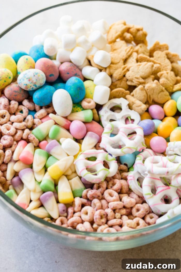Your Ultimate Easter Sunday Feast 7 Easter snack mix in a clear glass bowl with berry Cheerios, Easter candy corns, yogurt covered pretzels, Robin eggs, Easter M&Ms. mini marshmallows and bunny cookies.