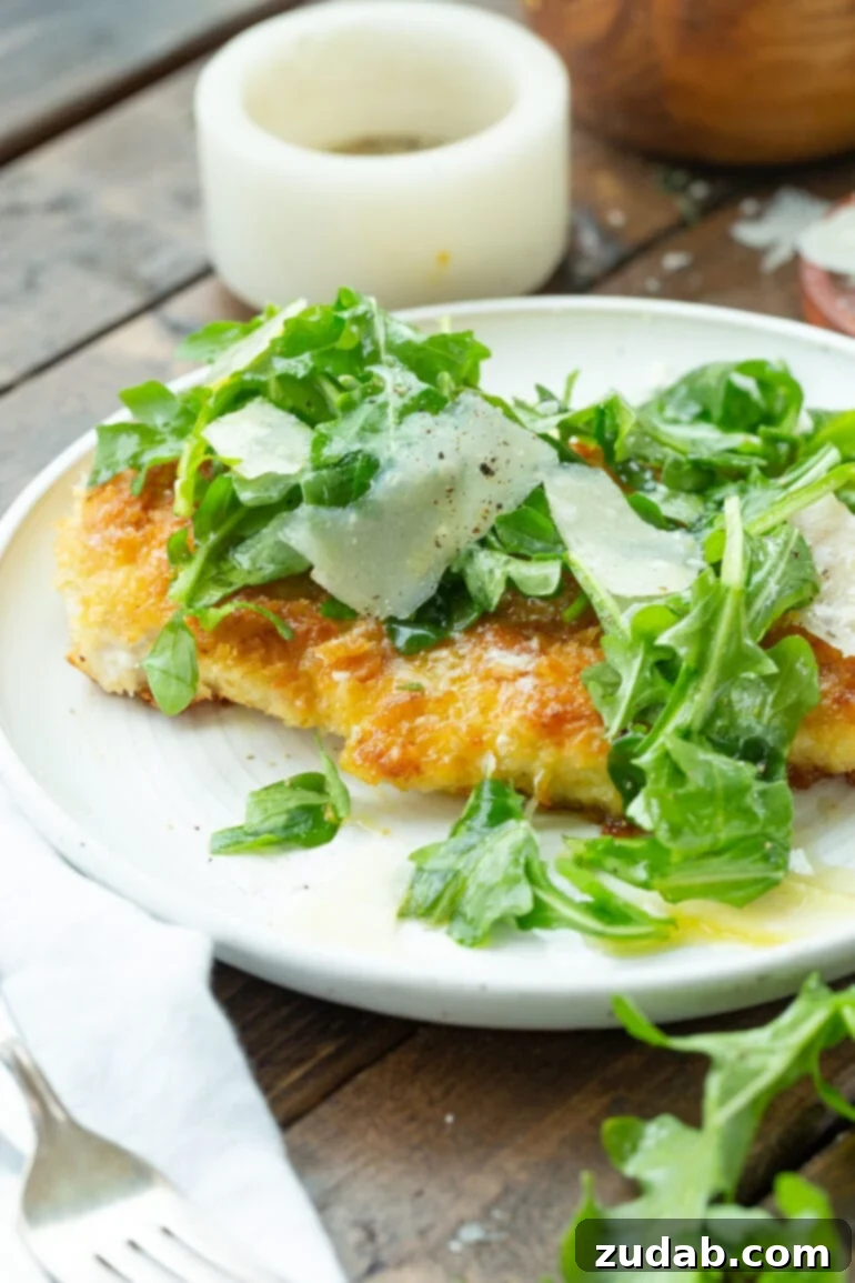 Your Weekly Meal Plan: May 6-12 3 A tantalizing photo of a golden, lightly breaded chicken breast, expertly prepared, resting on a pristine white dinner plate. It's elegantly garnished with a fresh medley of salad greens and delicate shavings of Parmesan cheese, offering a visually appealing and healthful meal.