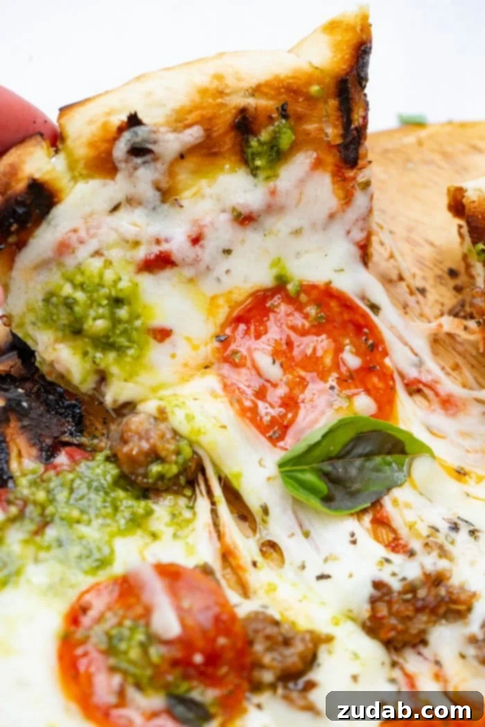 Your Weekly Menu: June 3-9 4 A mouth-watering close-up photo of a slice of Pesto Pepperoni & Sausage Grilled Pizza being pulled away, showing the crispy, smoky crust, melted Tillamook cheese, savory pepperoni, and vibrant pesto sauce.