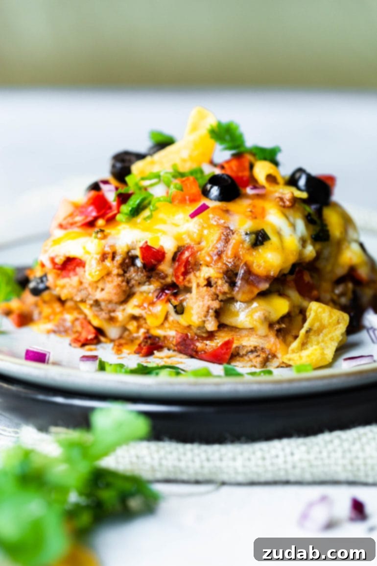 Your Weekly Menu: June 3-9 5 A close-up photo of a generous piece of Quick Weeknight Taco Casserole on a plate, showcasing layers of cheesy ground beef, melted cheese, black beans, diced tomatoes, and fresh cilantro garnish.