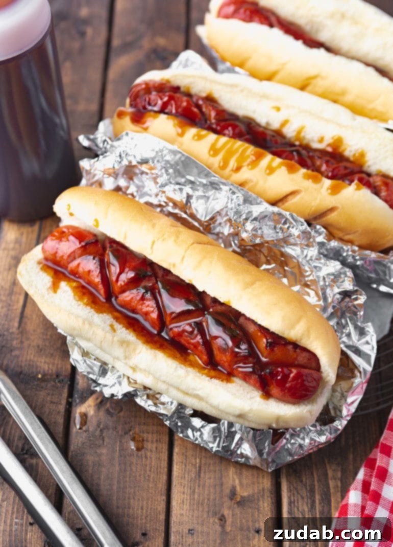 Your Weekly Menu: June 3-9 7 A close-up photo of a perfectly grilled hot dog, crisscross-sliced, nestled in a bun wrapped in aluminum foil, and generously covered in the signature J.Dawgs special sauce.