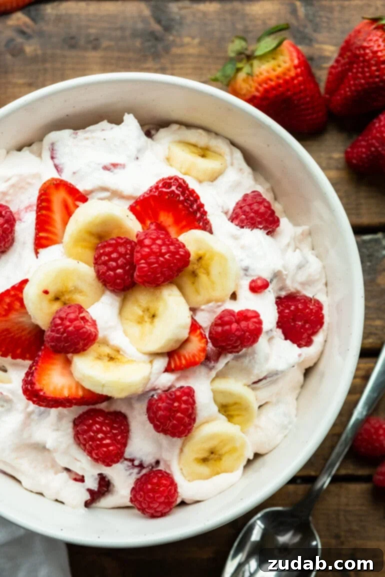 Fluffy Cheesecake Fruit Salad 2 a photo of a bowl of creamy cheesecake fruit salad topped with slices of banana and whole raspberry and sliced strawberries