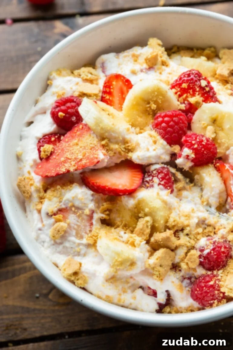 Fluffy Cheesecake Fruit Salad 3 a photo of a bowl of creamy cheesecake fruit salad with sliced bananas and strawberries and whole raspberries and chunks of crushed graham cracker.