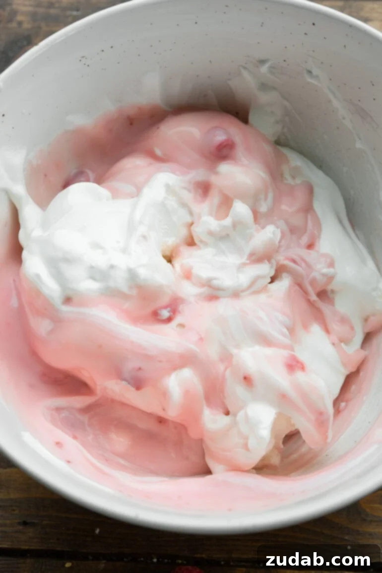 Fluffy Cheesecake Fruit Salad 5 a photo of a cheesecake pudding being stirred together with strawberry yogurt and Cool Whip