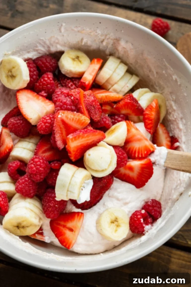 Fluffy Cheesecake Fruit Salad 6 a photo of sliced strawberries, bananas and whole raspberries being folded into a light pink creamy yogurt mixture