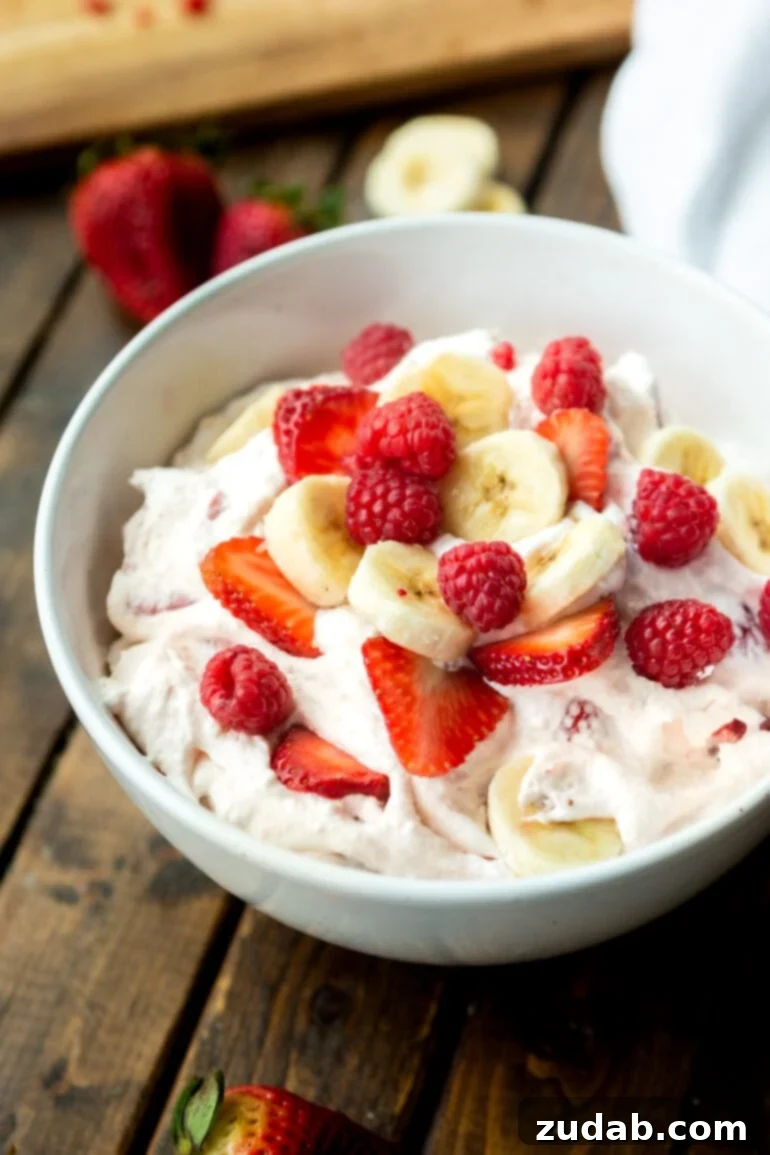 Fluffy Cheesecake Fruit Salad 7 a photo of a large bowl full of sliced bananas, strawberries and whole raspberries mixed with creamy yogurt and cheesecake pudding.