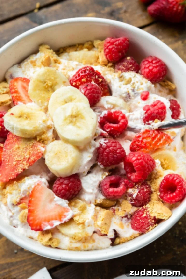 Fluffy Cheesecake Fruit Salad 9 a photo of a creamy fruit salad with bananas, strawberries and raspberries topped with crushed graham crackers