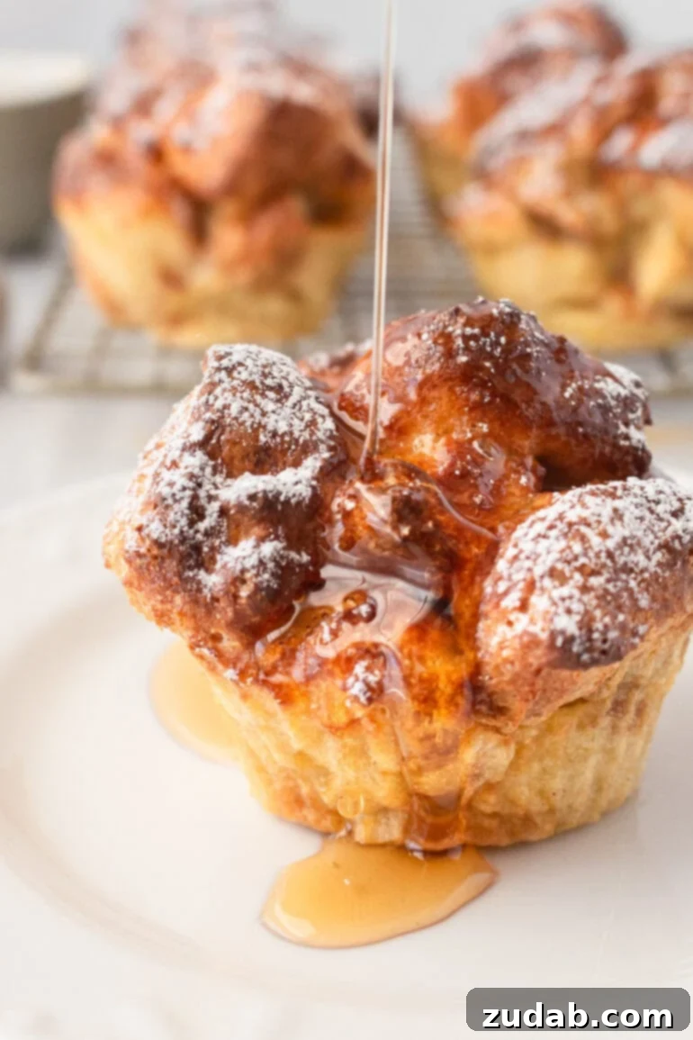 a photo of syrup being drizzled over a golden french toast muffin dusted with powdered sugar