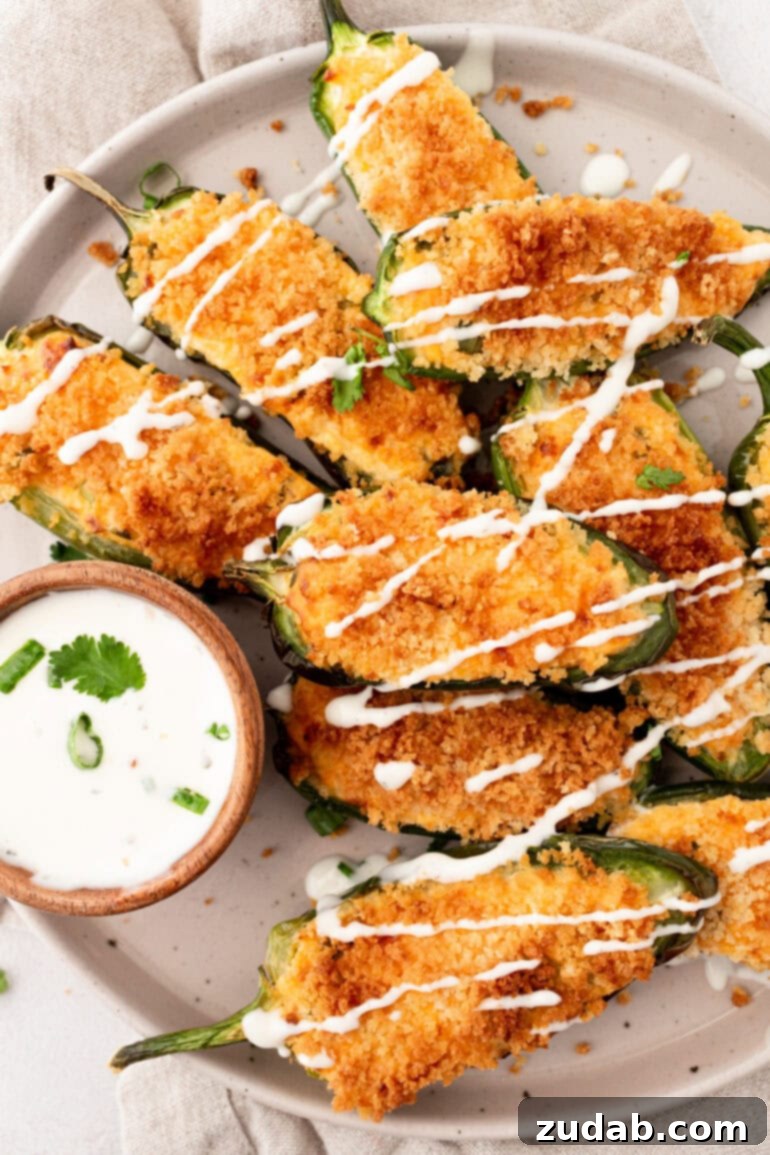 Effortless Air Fryer Jalapeño Poppers 2 A photo of golden crispy jalapeno poppers sitting on a plate next to a small cup of ranch dip