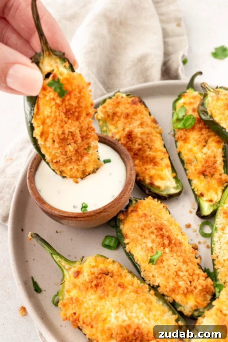 Effortless Air Fryer Jalapeño Poppers 3 A photo of someone dipping a golden crispy jalapeno popper into a little cup of ranch dressing