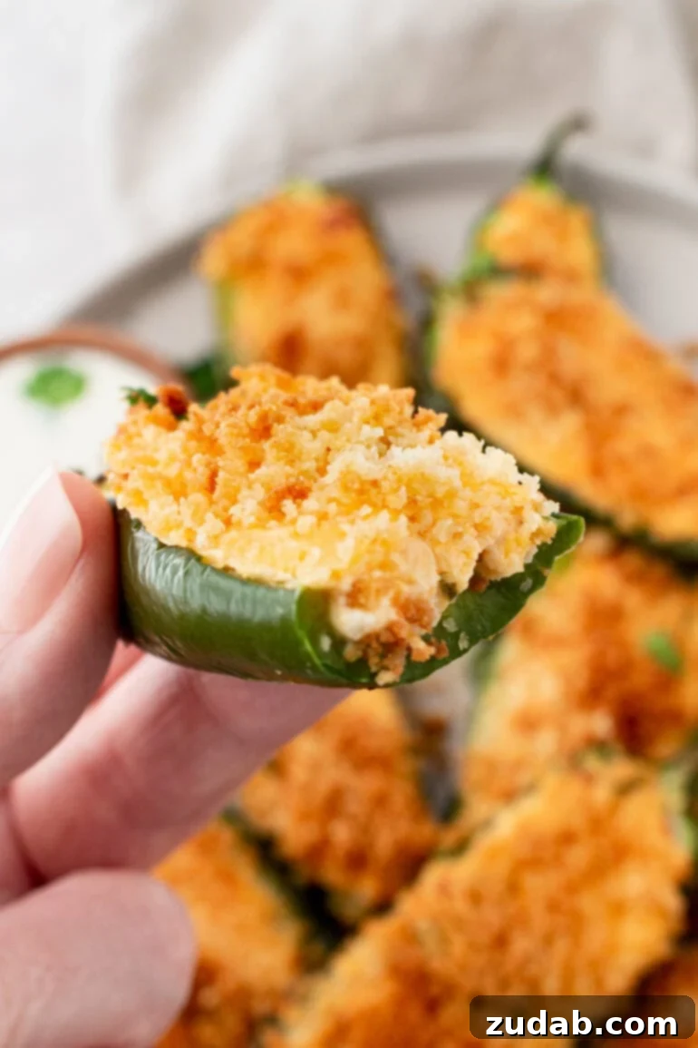 Effortless Air Fryer Jalapeño Poppers 8 A photo of someone holding a golden crispy jalapeno popper that someone has taken a bite out of with more whole ones in the background