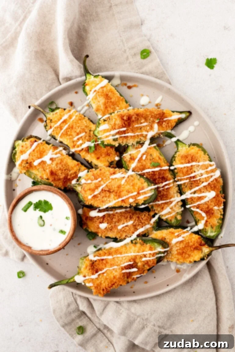 Effortless Air Fryer Jalapeño Poppers 9 A photo of a plate full of crispy golden jalapeno poppers drizzled with garlic sauce