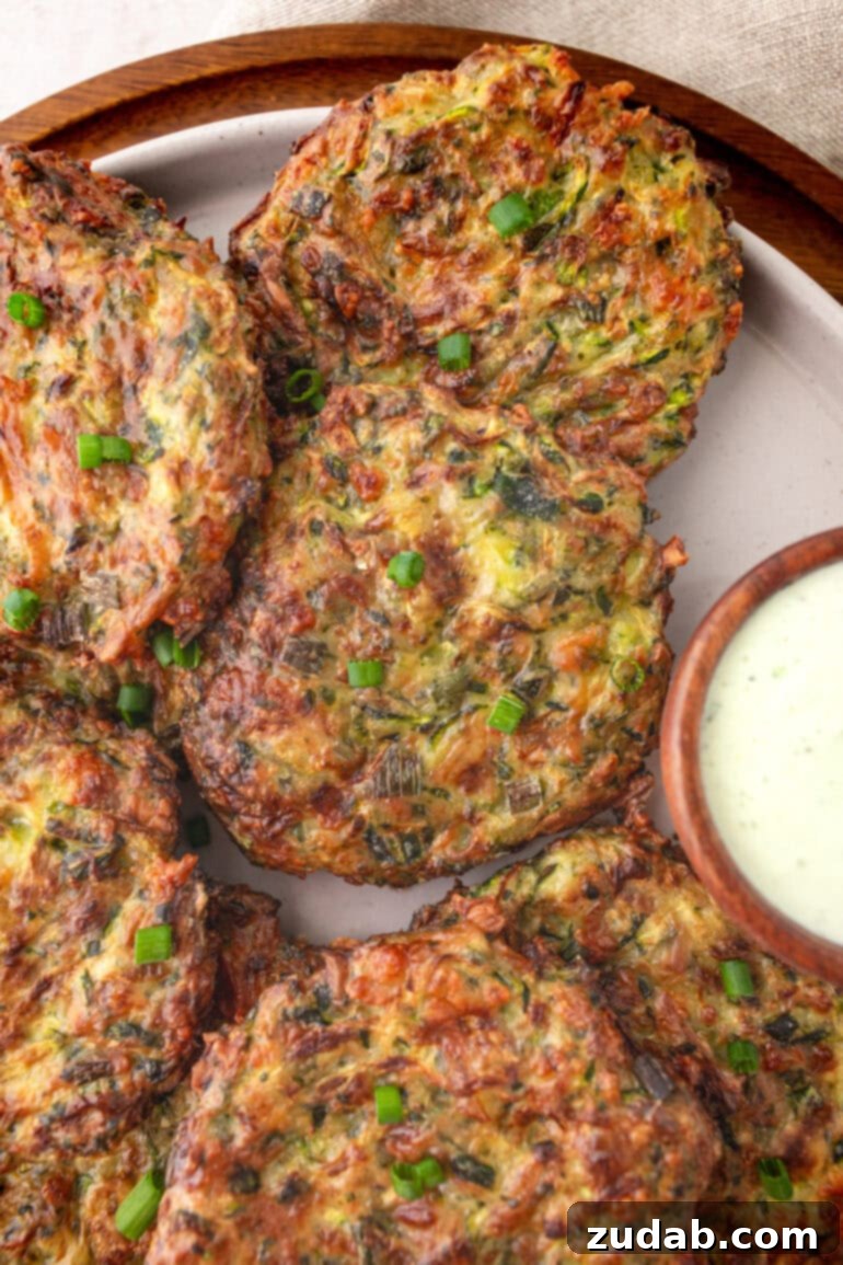 a photo of several golden fried zucchini fritters sitting next to a small cup of creamy dipping sauce