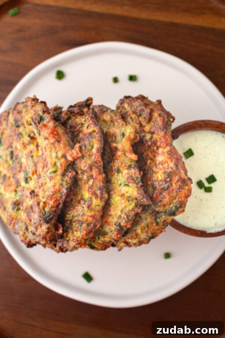 a photo of four zucchini fritters stacked on their side leaning up against a cup of dipping sauce