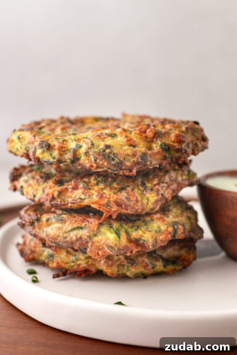 a photo of a stack of 4 crispy zucchini fritters sitting next to a small bowl of creamy white dipping sauce