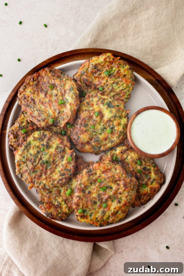 a photo of several crispy golden zucchini fritters sitting on a plate sitting next to a small dish of creamy dipping sauce