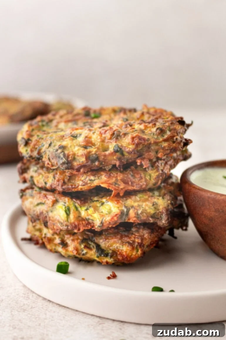 a photo of four zucchini fritters stacked on each other sitting next to a cup of dipping sauce