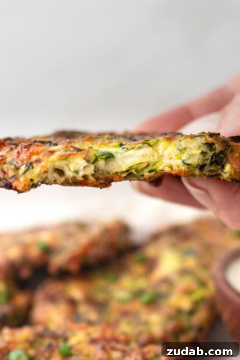 a photo of a someone holding a single zucchini fritter  with a bite out of is so you can see the cheesy inside.