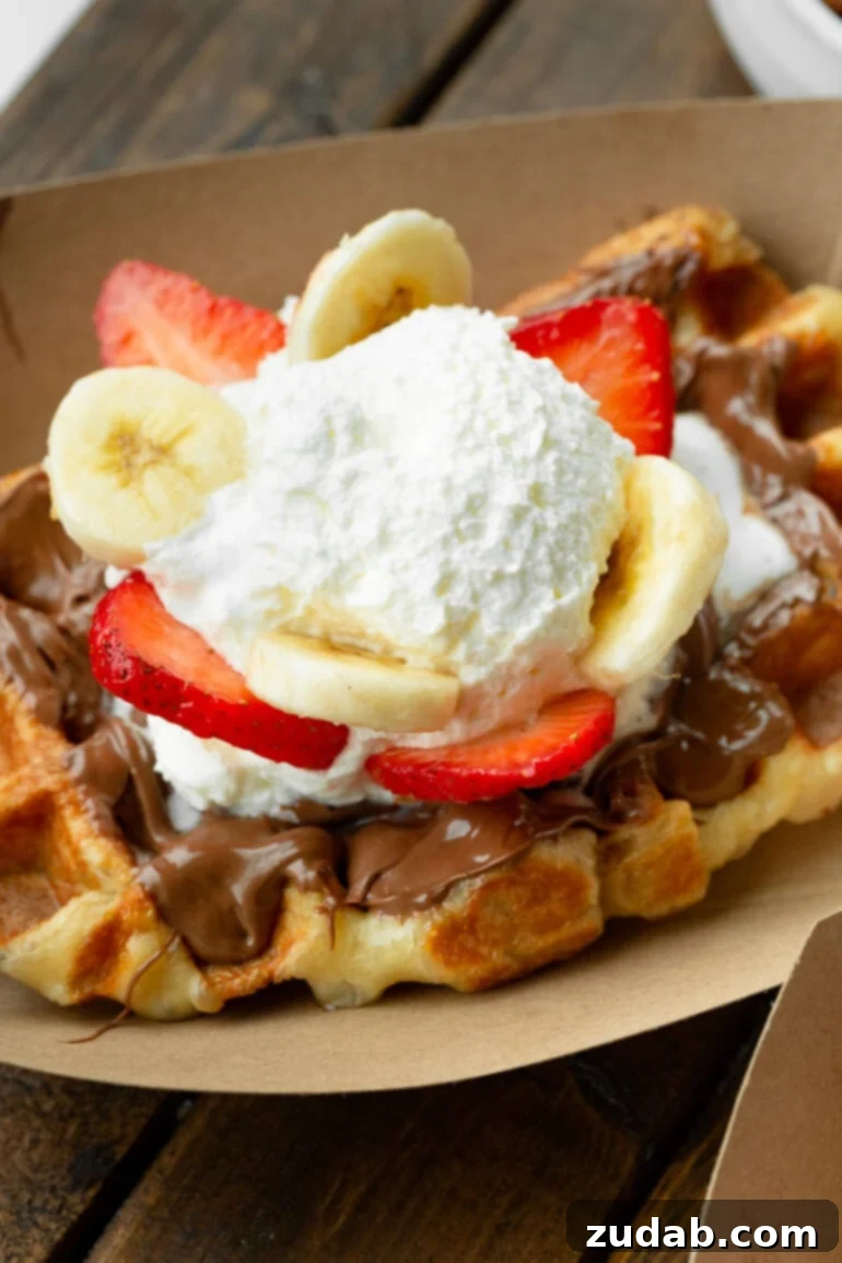 Mastering Waffle Love's Signature Liege Waffles 2 A photo of a golden Liege waffle in a brown cardboard carton topped with Nutella, sliced strawberries and bananas, and whipped cream. The perfect Waffle Love copycat.