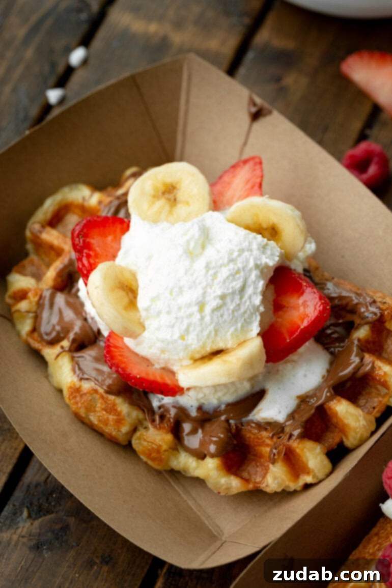 Mastering Waffle Love's Signature Liege Waffles 5 A photo of a large Liege waffle topped with melting Nutella, sliced strawberries and bananas, and a dollop of creme fraiche. A vibrant and delicious Liege waffle topping idea.