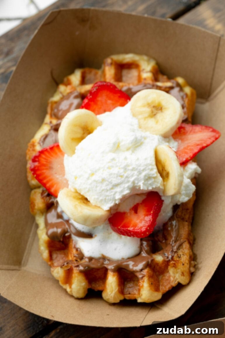 Mastering Waffle Love's Signature Liege Waffles 8 A photo taken over the top of a golden Liege waffle topped with Biscoff cookie butter, sliced strawberries and bananas, and whipped cream. A delightful and satisfying treat.