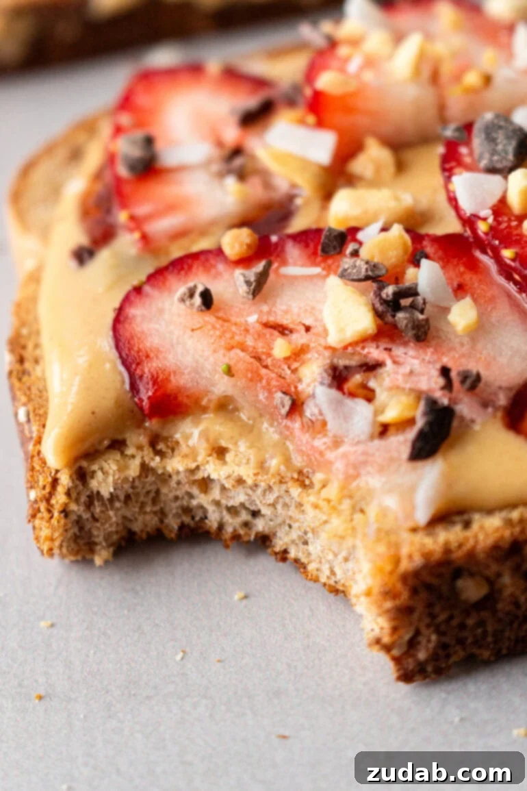 Creamy Coconut Peanut Bliss 3 A piece of multigrain toast generously topped with homemade coconut peanut butter, fresh strawberry slices, and a sprinkle of granola crumble.