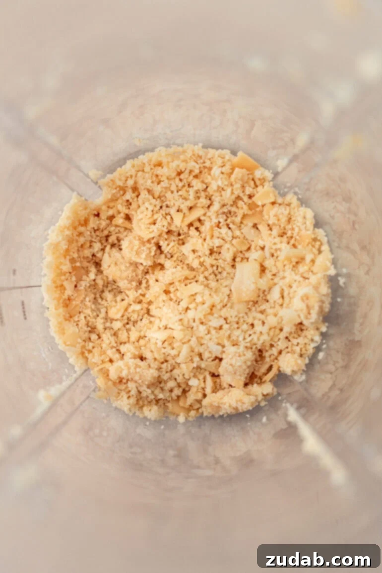 Creamy Coconut Peanut Bliss 5 A close-up shot of coconut chips being blended in a food processor, showing the initial grainy stage of the process.