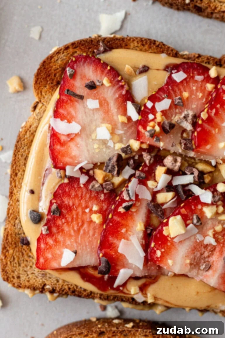 Creamy Coconut Peanut Bliss 10 A piece of toast topped with coconut peanut butter, sliced strawberries, and a sprinkle of chocolate bits, chopped peanuts, and coconut flakes.