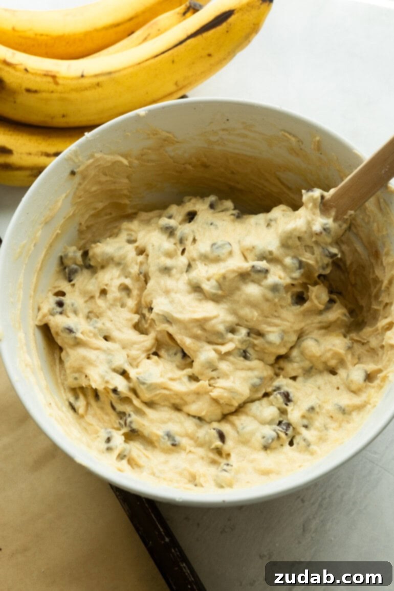 Golden Banana Chocolate Chip Delights 6 A large mixing bowl filled with creamy banana chocolate chip cookie dough being gently stirred with a wooden spoon, indicating the final stage of dough preparation.