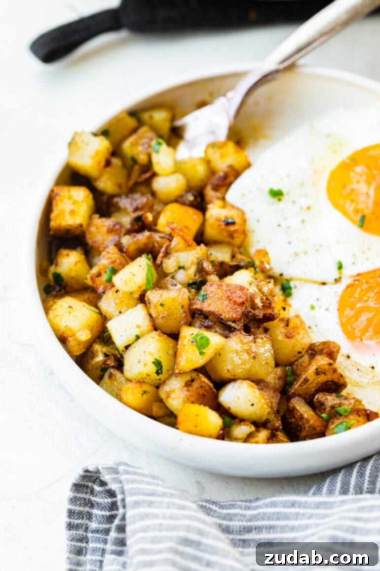 Ultimate Home Fries Recipe 6 A close-up photo of a dish of golden, crispy home fries served alongside two fried eggs, showcasing a delicious and satisfying breakfast or brunch.