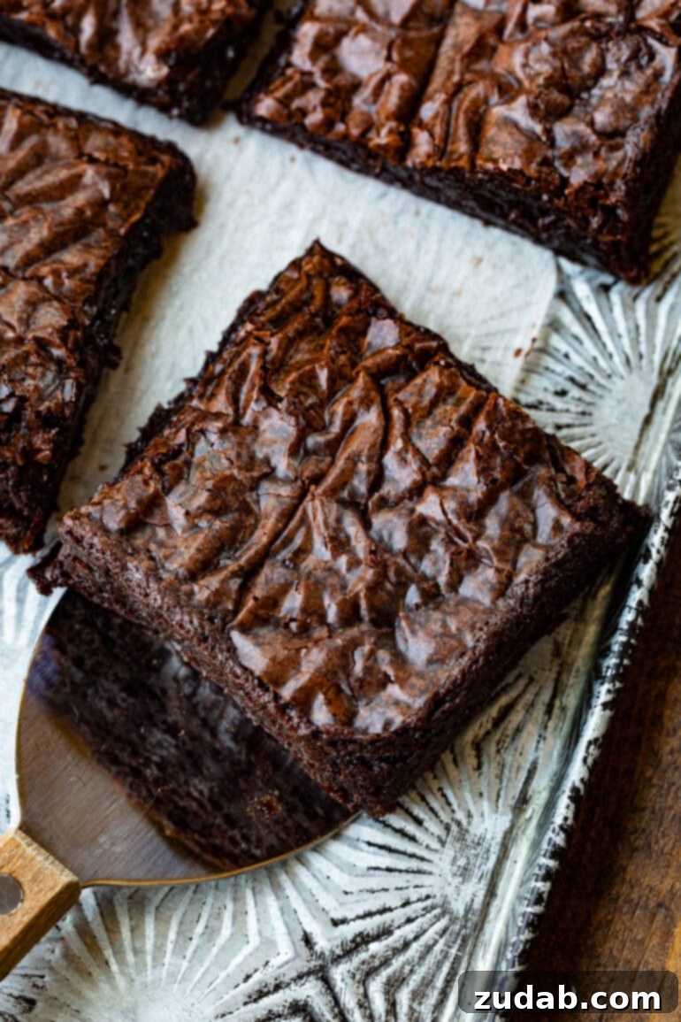Elevated Box Brownies 3 A perfectly sliced square of fudgy chocolate brownie being carefully lifted from a baking pan with a small metal spatula, highlighting its dense, moist texture.