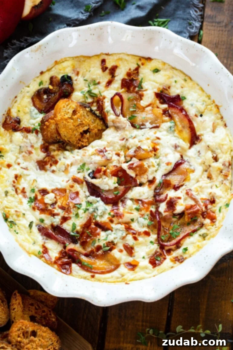 Sweet Pear, Savory Prosciutto & Tangy Blue Cheese Dip 2 A top-down photo of a circular ceramic baking dish filled with roasted pear blue cheese dip, garnished with fresh herbs.