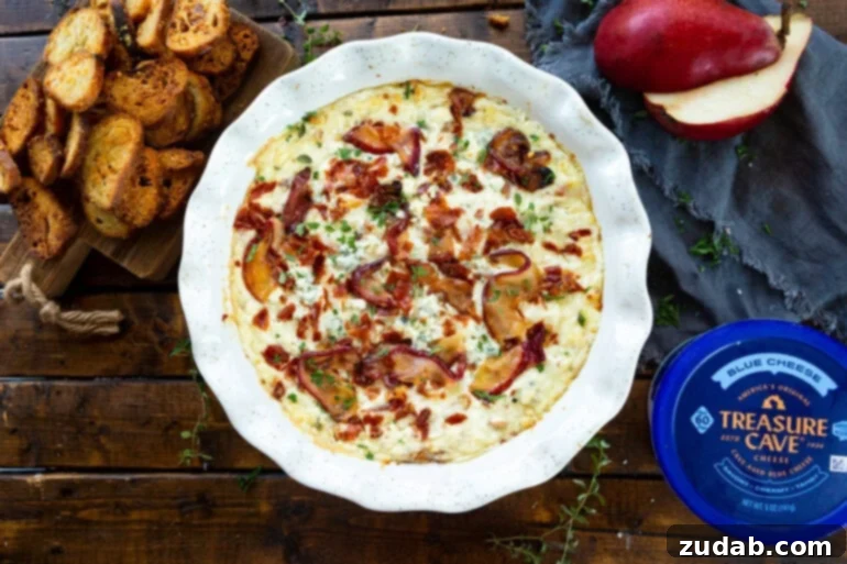 Sweet Pear, Savory Prosciutto & Tangy Blue Cheese Dip 9 A top-down photo of a circular ceramic dish filled with blue cheese dip topped with roasted pears and crispy prosciutto, with a container of Treasure Cave blue cheese alongside.