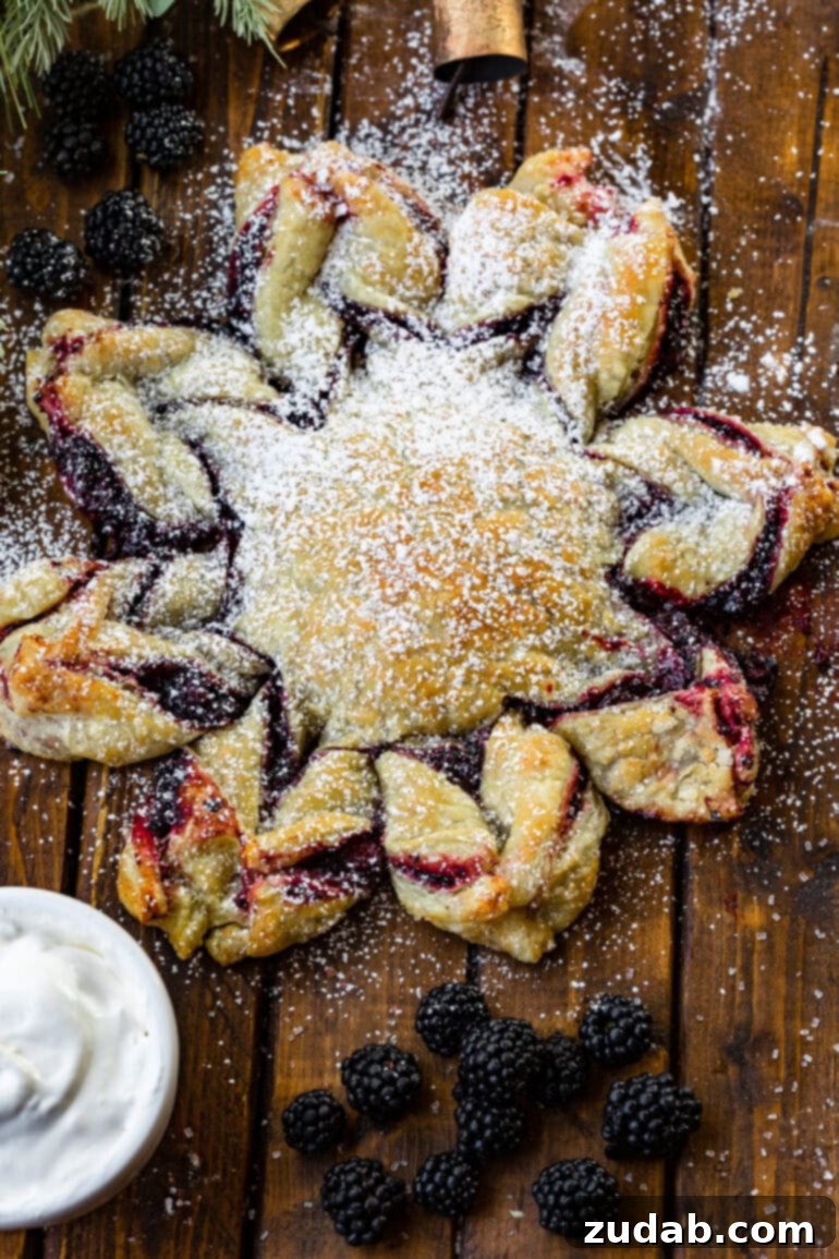 Blackberry Snowflake Puff Pastry 2 A beautifully baked blackberry puff pastry snowflake, lightly dusted with powdered sugar, with fresh whole blackberries scattered around it on a rustic surface.