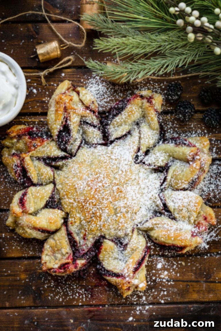 Blackberry Snowflake Puff Pastry 8 An overhead shot of a perfectly golden-baked blackberry puff pastry snowflake, exquisitely dusted with a fine layer of powdered sugar.