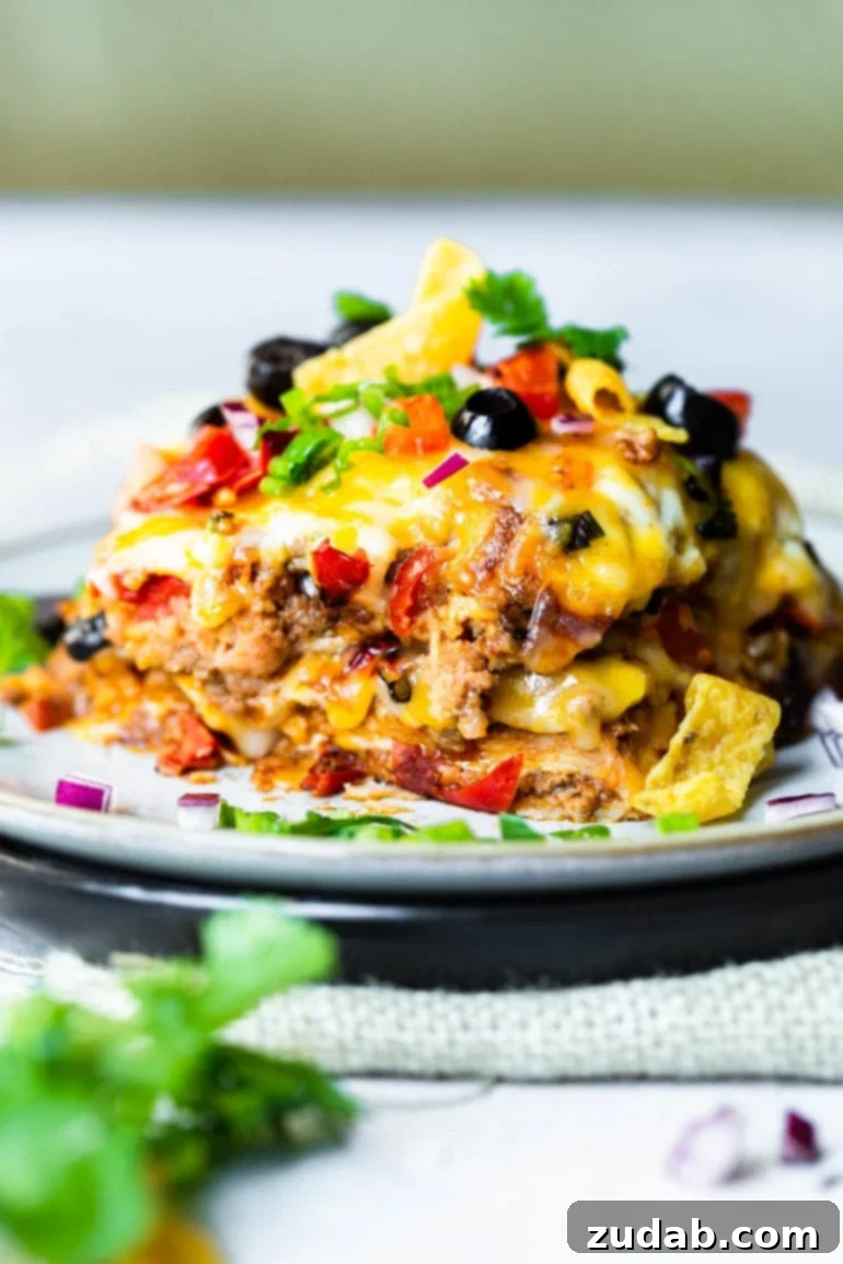 This Week's Meal Plan: September 23-29 7 A close-up photo of a generous piece of Taco Casserole served on a saucer, showcasing its delicious layers of cheesy ground beef, black beans, diced tomatoes, and a molten cheese topping, garnished with fresh cilantro.