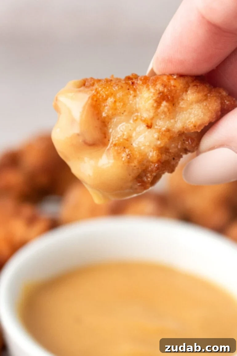 A close-up photo of a golden, crispy chicken nugget freshly dipped into a small bowl of creamy orange Chick-fil-A sauce, highlighting its delicious texture.
