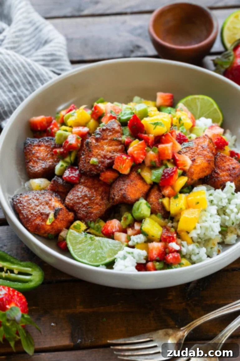 Golden Crispy 7-Minute Air Fryer Salmon Bites with Zesty Mango Salsa 2 A beautifully presented bowl of crispy air fryer salmon bites, nestled on a bed of rice and generously topped with a colorful strawberry mango avocado salsa.